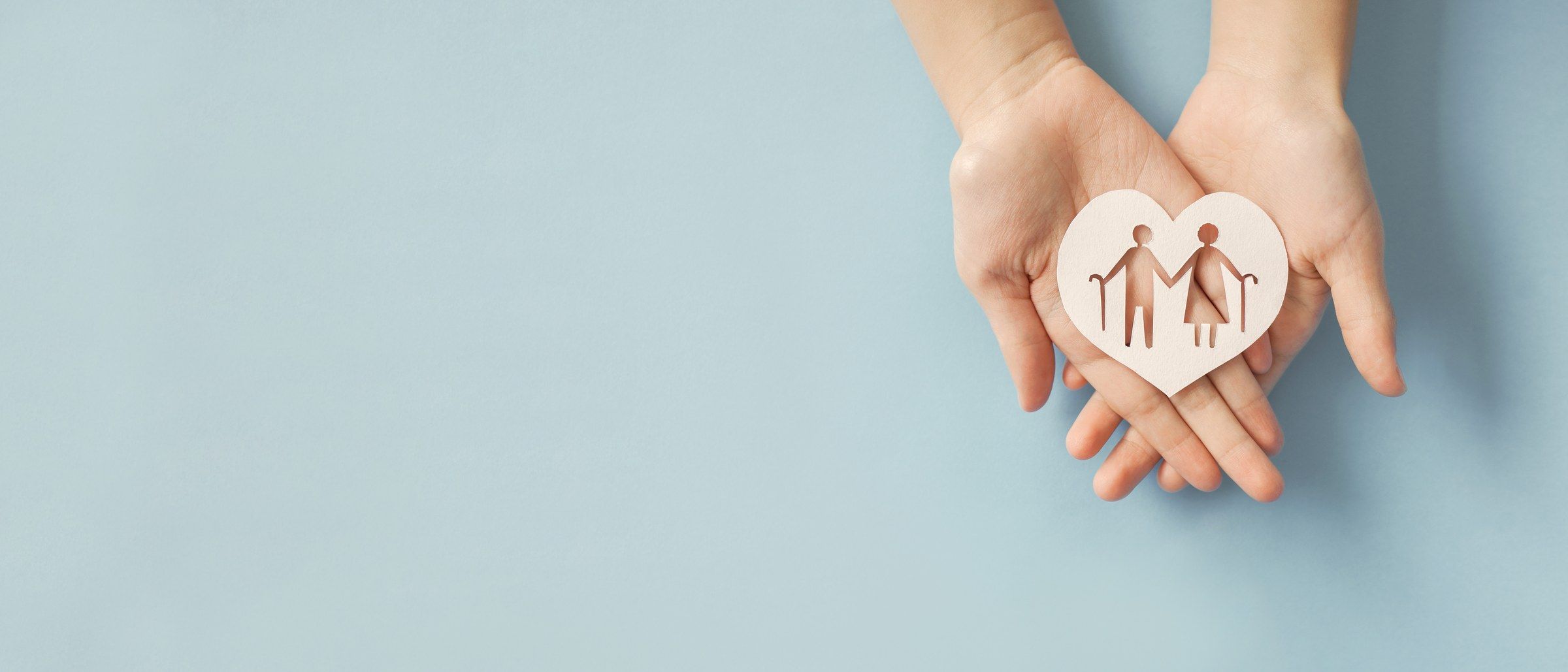 Two open hands holding a paper heart with an older couple cut out of it.