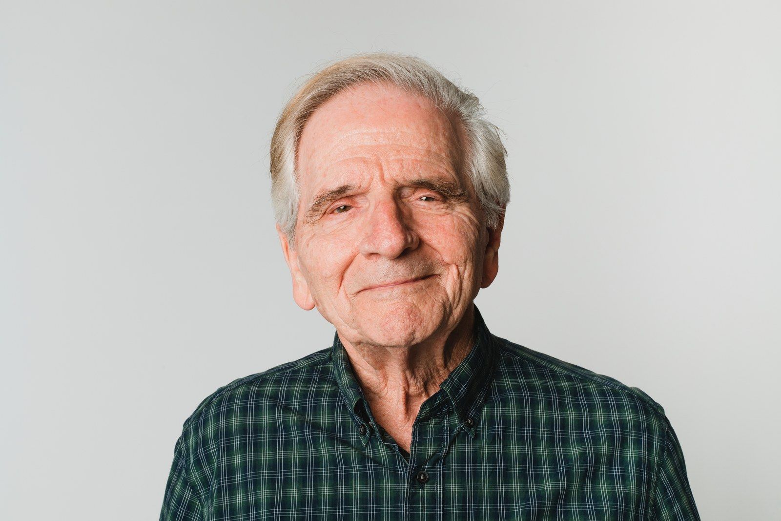 An older man in a green plaid shirt looking directly at the camera.